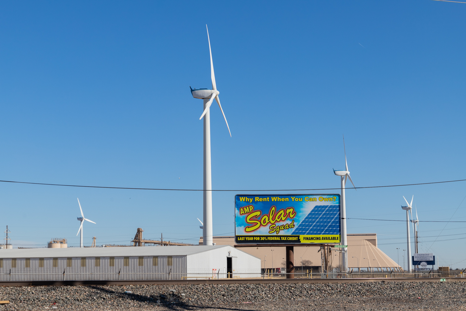 Wind turbines located at the local Cotton Cooperative in Lubbock, Texas spin behind a billboard promoting solar energy. (Codi Clark/Texas Tech University)